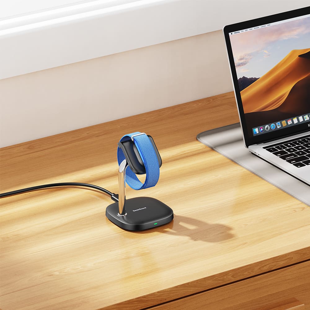 Fitbit Air charging on a compact fitbit charger wireless charging station on an office desk next to a laptop with SwanScout S10034FA